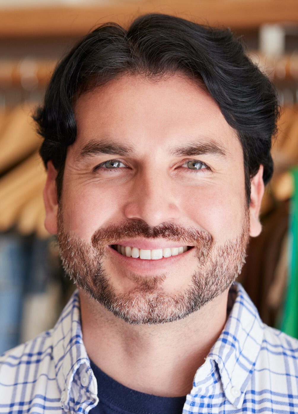 Portrait Of Smiling Male Owner Of Fashion Store Standing In Front Of Clothing On Rails